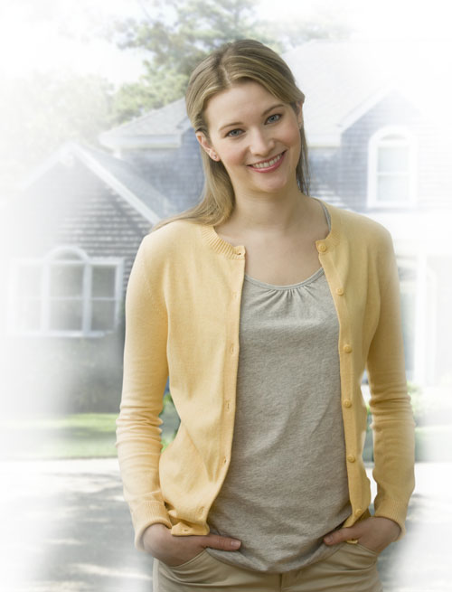 A young woman is standing outside in a residential neighborhood and smiling at the camera. Vertical shot.